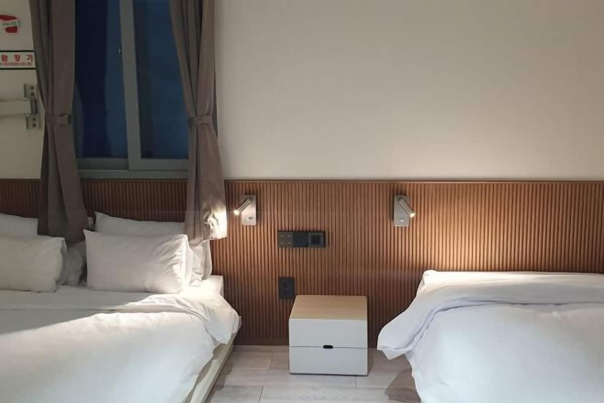 A hotel room with two beds, a wooden headboard, a bedside table, and a window with curtains.