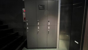 A set of six dark-colored, numbered lockers with a red emergency button and a small sign above the door. - Hotel Regen (Seoul)