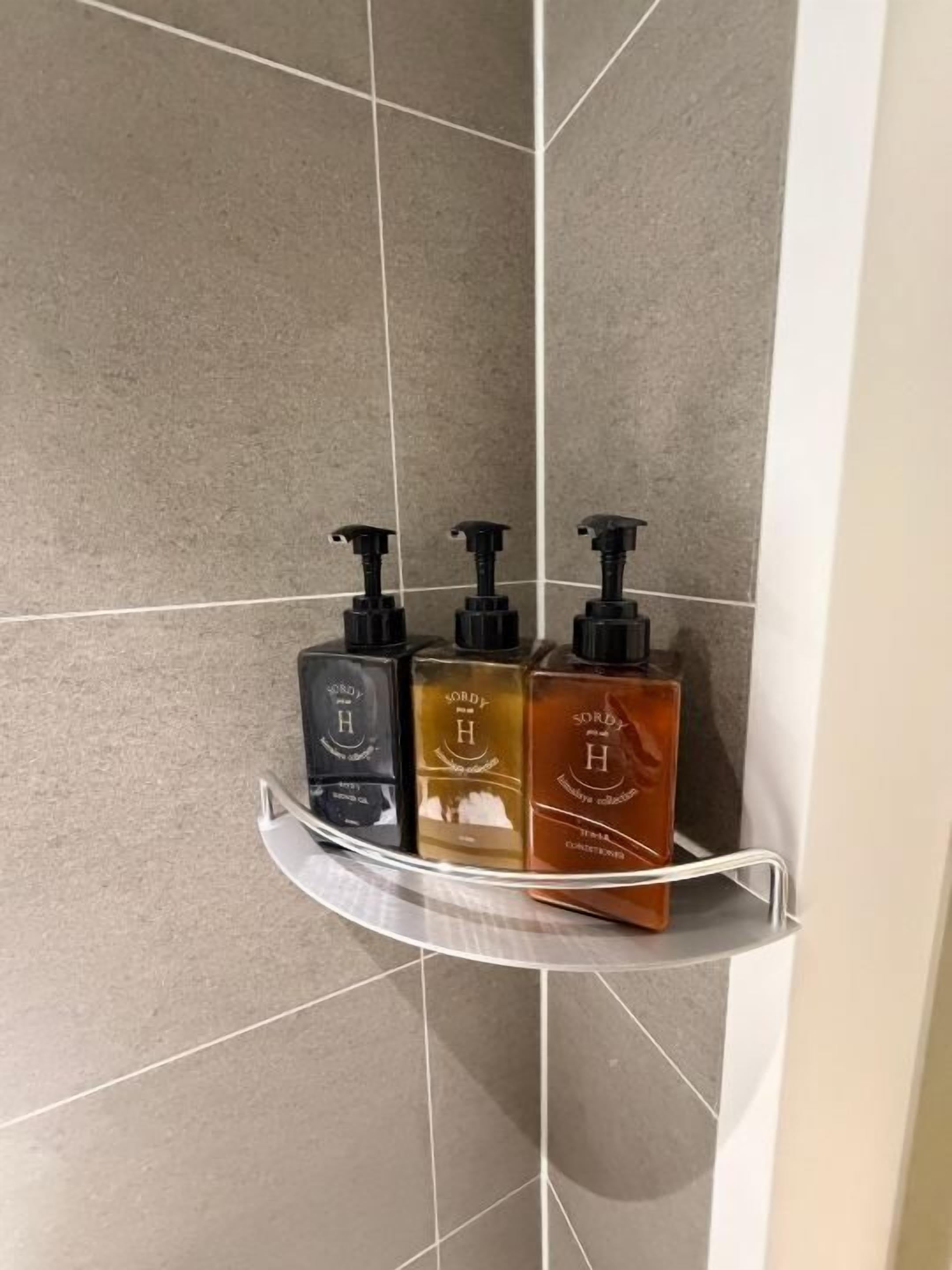 Uma área de chuveiro com três frascos de sabonete líquido em uma prateleira.