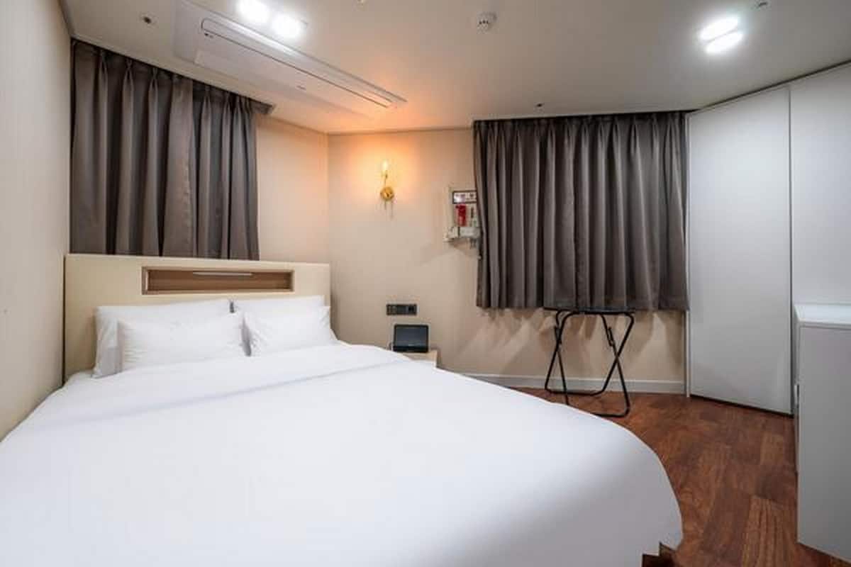 A hotel room with a large bed, a nightstand, a lamp, and a window with curtains.
