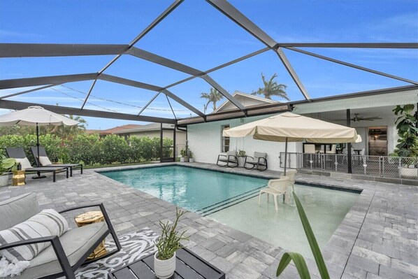 A covered outdoor swimming pool with lounge chairs, a sofa, and umbrellas.