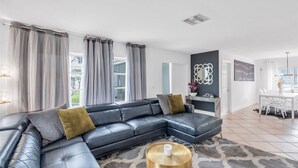 En moderne stue med en hjørnesofa, et spiseområde med et hvidt bord og stole, og et køkken i baggrunden.