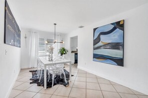 A modern dining area with a white table, clear chairs, a black rug, and a large abstract painting on the wall.