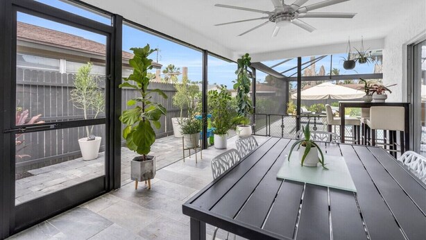 En overdækket terrasse med et bord, stole, plantekasser og en ventilator i loftet.