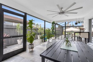 A covered patio with a table and chairs, potted plants, and a ceiling fan.