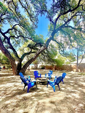 A backyard with a fire pit and blue chairs arranged around it, surrounded by large trees. - Charming 3-bedroom in Canyon Lake with Fire Pit , BBQ, WiFi and AC (Canyon Lake)