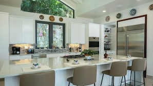 A modern kitchen with a central island, white cabinetry, a large refrigerator, and a window overlooking greenery.