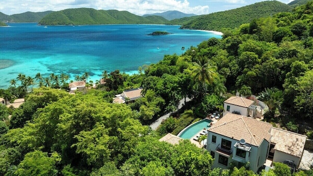 A tropical resort with a swimming pool, lush greenery, and a view of the ocean.