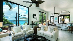 A spacious living room with large windows, a ceiling fan, and a view of the ocean.