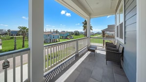 A covered porch with a view of a residential area, including houses and a green lawn. - Beachside Serenity | Modern, Near the Beach (Galveston)