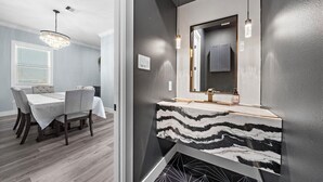 A modern bathroom with a marble countertop and a large mirror. - Beachside Serenity | Modern, Near the Beach (Galveston)