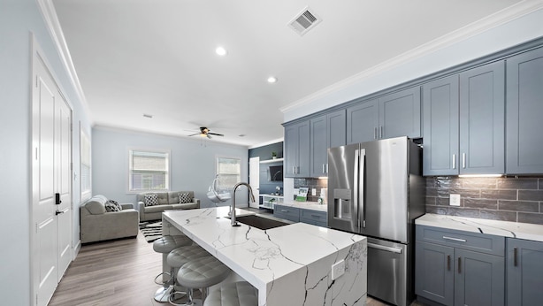 A modern kitchen with grey cabinets, a white marble island, stainless steel appliances, and a bar area with stools. - Beachside Serenity | Modern, Near the Beach (Galveston)