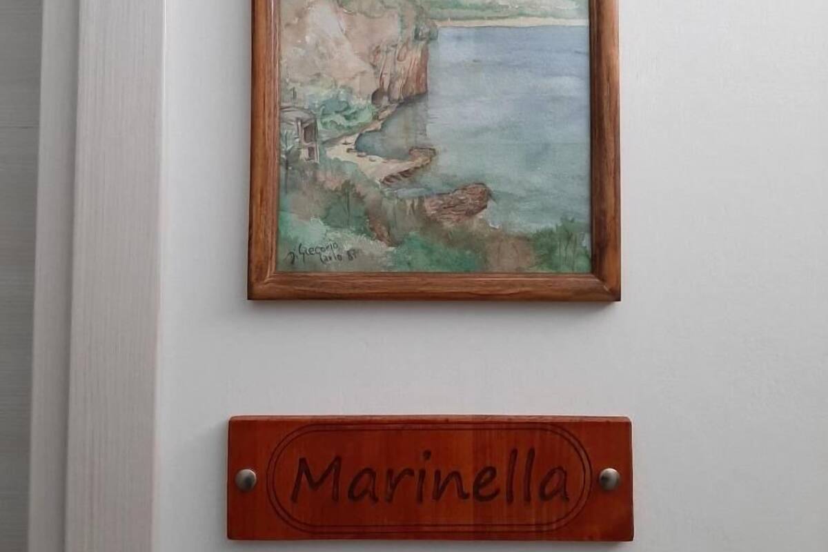 A framed painting of a coastal scene with cliffs and a body of water, and a wooden nameplate below it with the name "Marinella".