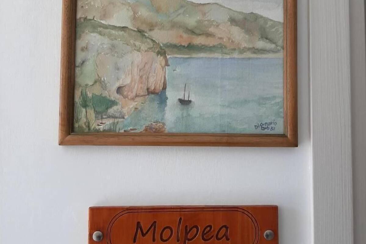 A framed painting of a coastal scene with cliffs and a boat, and a wooden plaque with the name "Molpea" below it.