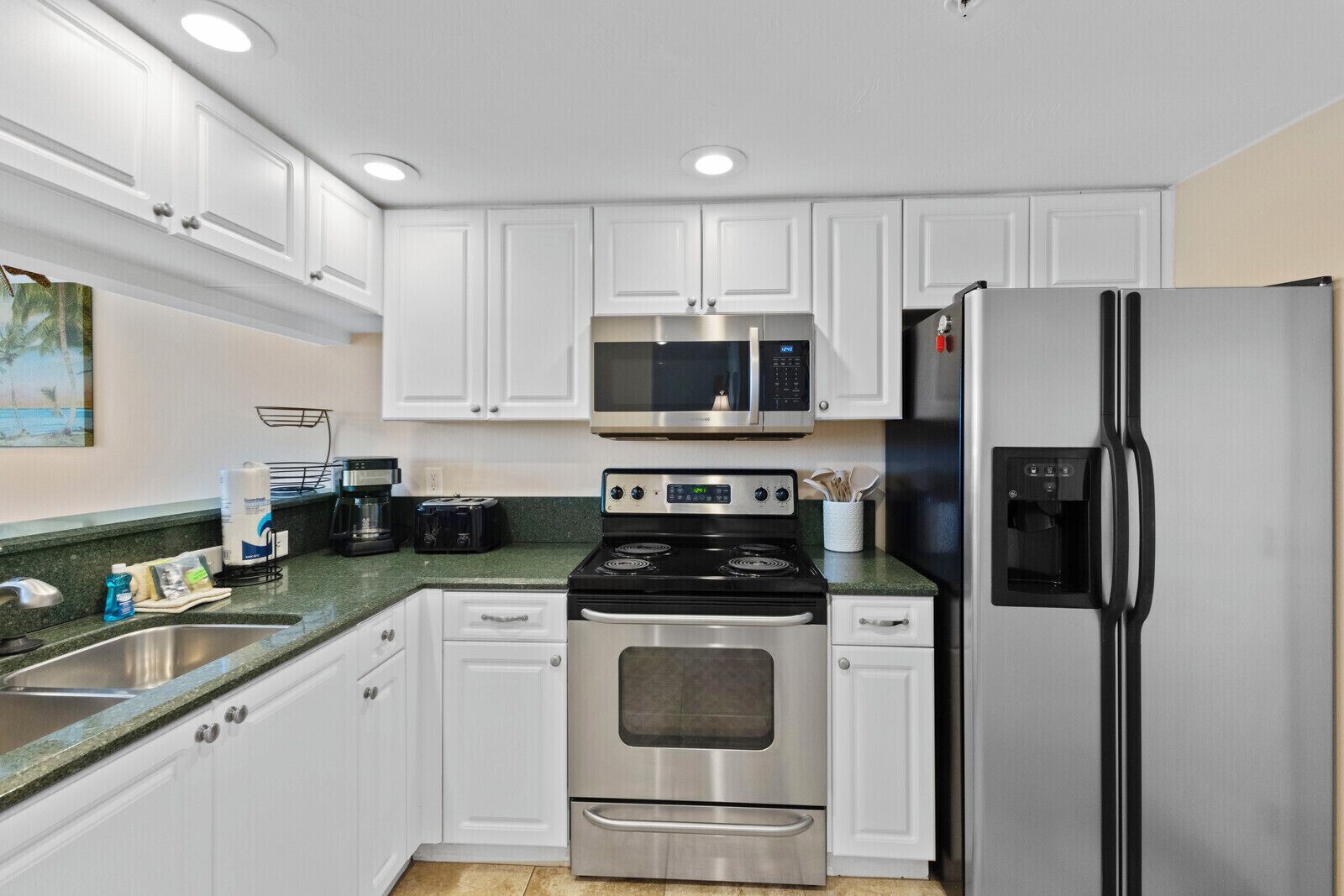 Una cocina moderna con armarios blancos, electrodomésticos de acero inoxidable, un microondas, una estufa y un refrigerador.