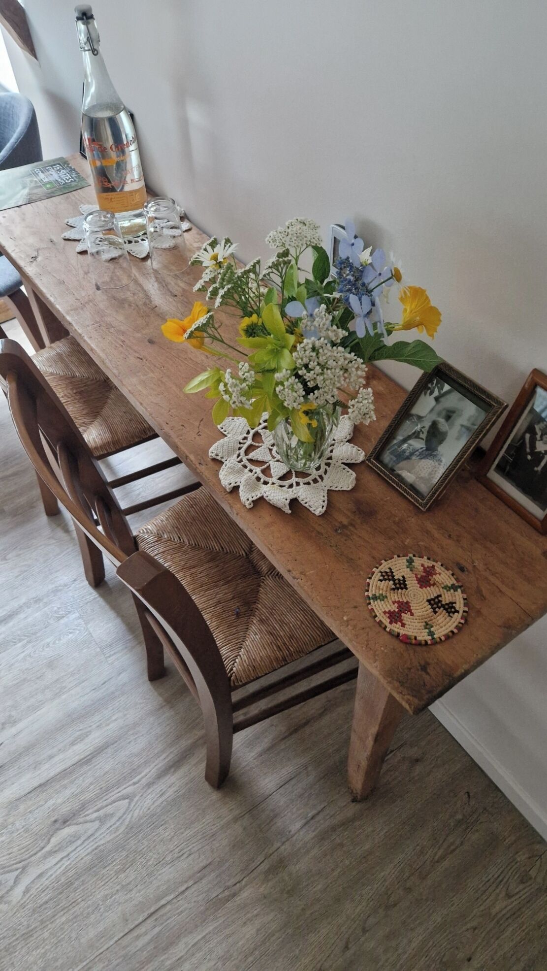 A wooden dining table with a vase of flowers, a bottle, and a framed photo.