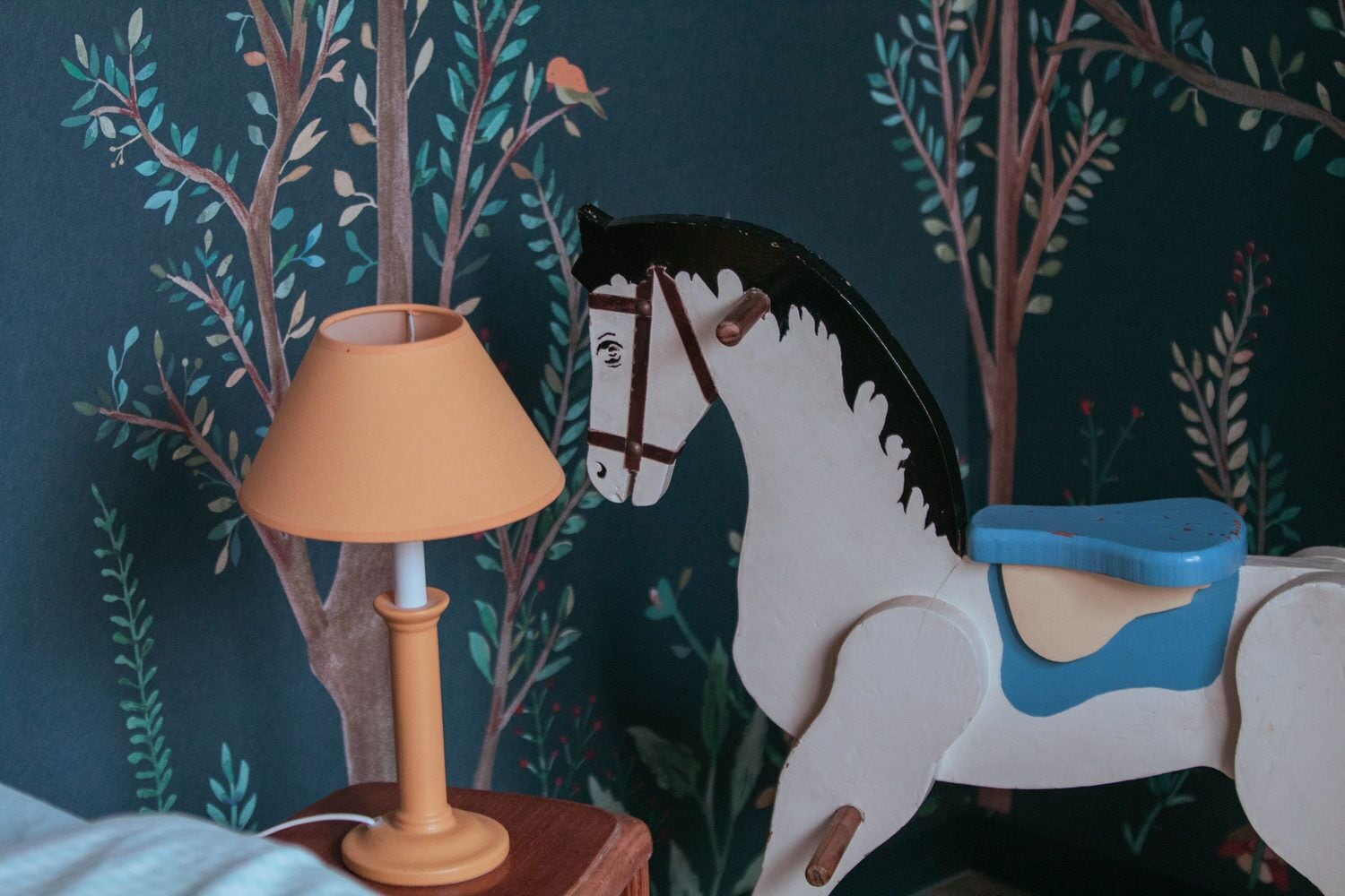 A wooden horse toy with a saddle and a lamp on a table.