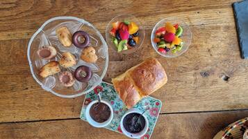 Una mesa de madera con diversos alimentos, incluyendo pasteles, hogaza de pan y ensalada de frutas.