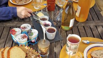 Una mesa de madera dispuesta con diversos alimentos, como pan, frutas y salsas, sugiriendo un picnic o comida al aire libre.