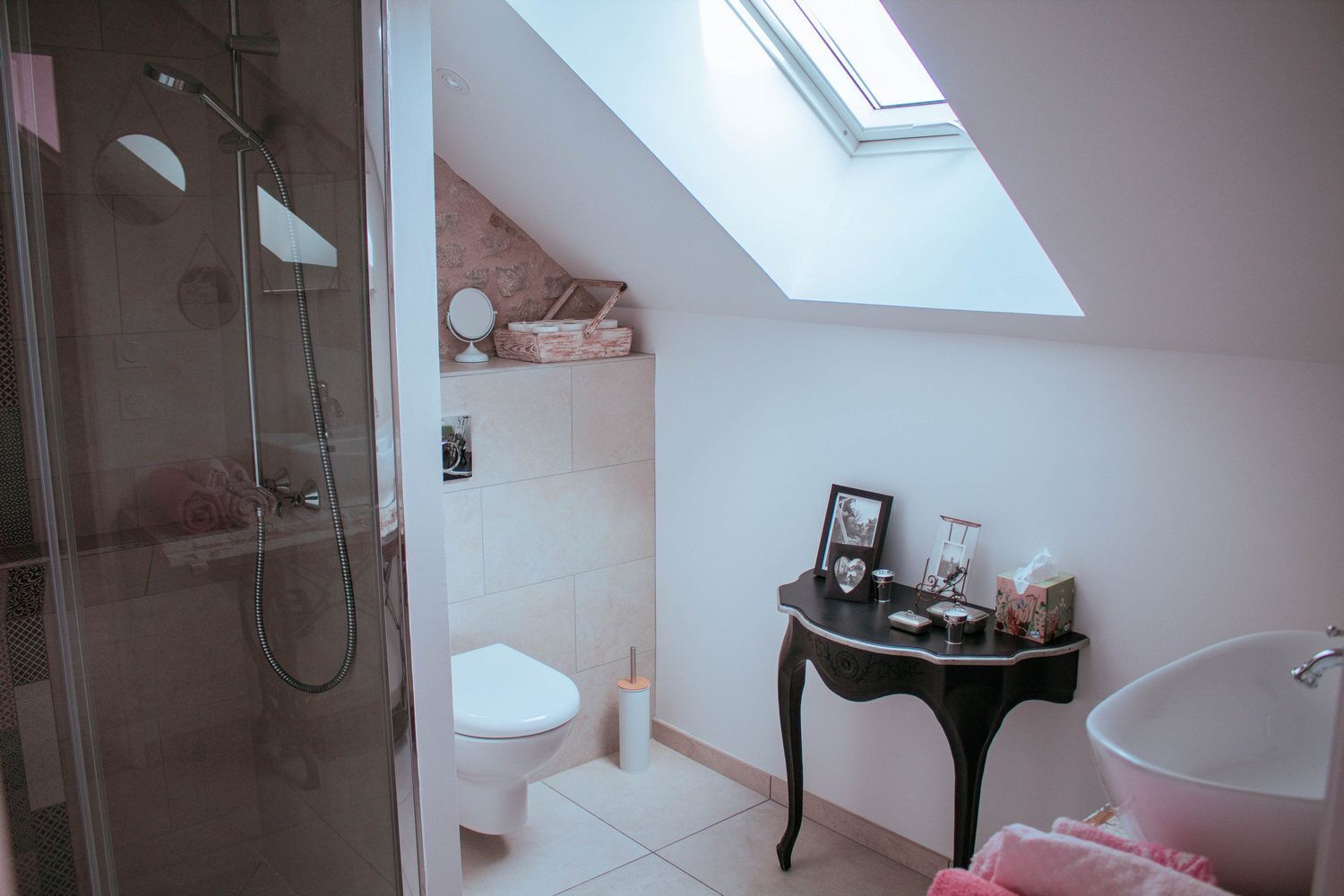 A modern bathroom with a skylight, a glass-enclosed shower, a white toilet, and a black vanity with toiletries.
