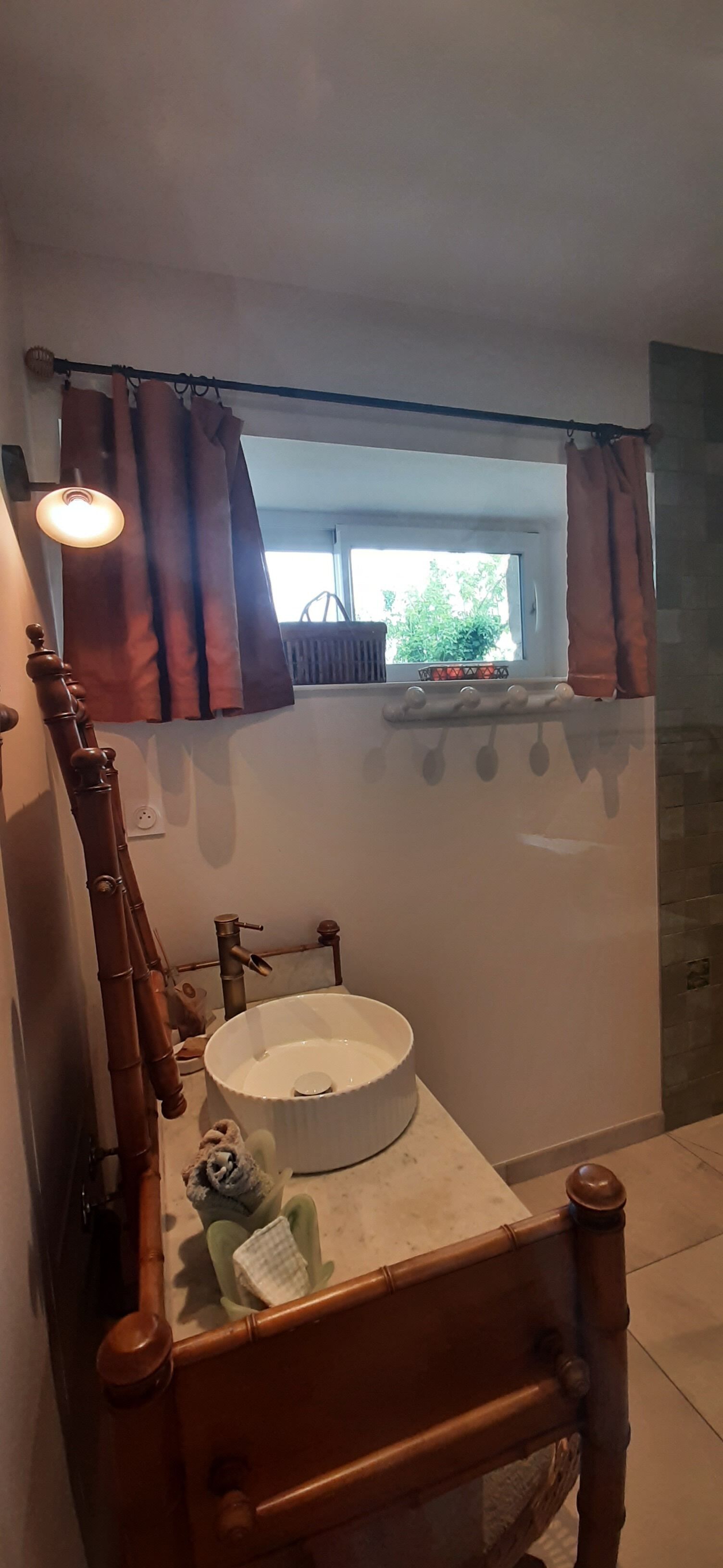 A bathroom with a wooden chair, a round sink, a window with curtains, and a radiator.