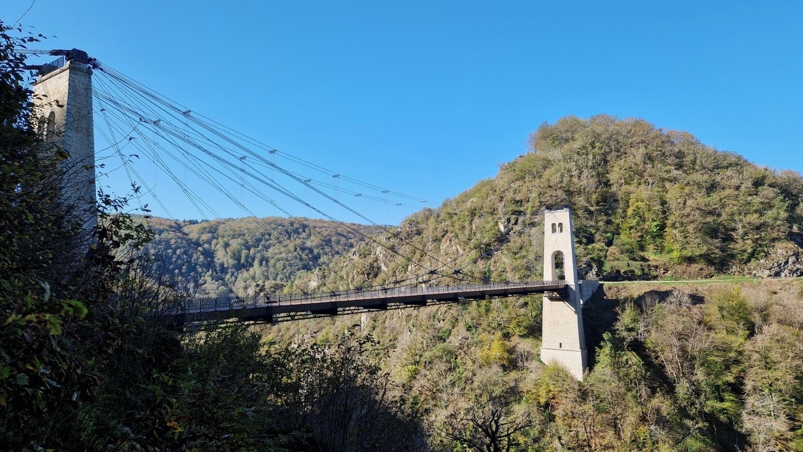 Un ponte sospeso con una torre, circondato da colline boscose.