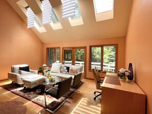 Relax in this spacious living area with a high ceiling, comfortable seating, and large windows offering a view of the outdoors.