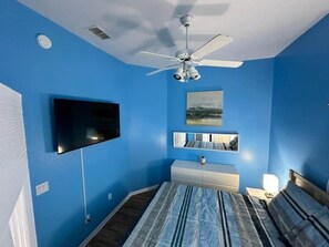 Un dormitorio con cama, ventilador de techo, televisor de pantalla plana, cómoda y espejo.