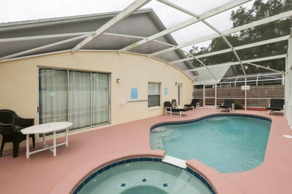 Piscina exterior cubierta con sillones de descanso y una mesa, rodeada por un edificio con puerta corrediza de vidrio.