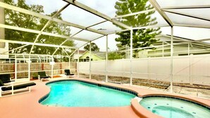 A swimming pool with a glass enclosure, surrounded by lounge chairs and a hot tub.