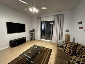 A living room with a flat-screen TV, a sofa, a coffee table, and a ceiling fan.