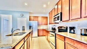 Eine Küche mit Holzschränken, Granit-Arbeitsplatten, einer Edelstahl-Spüle, einem Kühlschrank, einer Mikrowelle, einem Herd und einer Kaffeemaschine.