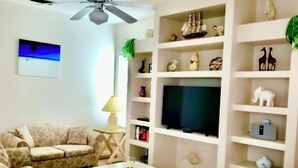 Sala de estar com sofá, mesa de centro, televisão e prateleiras com objetos decorativos.