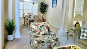 Uma sala de estar ampla com um sofá estampado, uma área de refeiç ões com mesa e cadeiras, e vista através de uma grande janela.