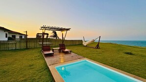 Un jardin avec une piscine, une terrasse en bois, des chaises longues et un hamac.
