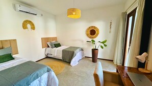 Une chambre d’hôtel avec deux lits, un bureau, un ordinateur portable, une plante en pot et une grande fenêtre avec des rideaux.