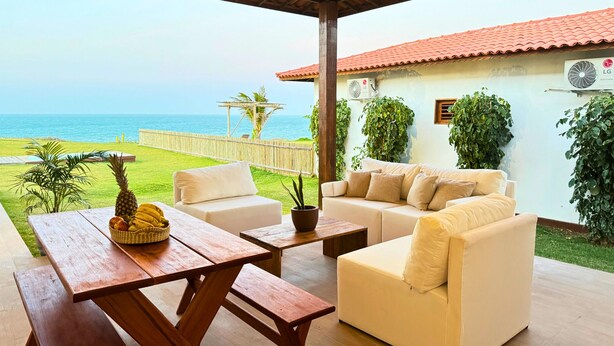 Une terrasse avec un canapé blanc, une table en bois et des chaises, donnant sur une plage.