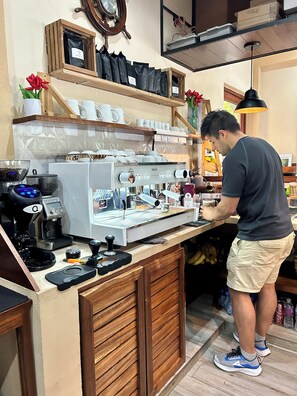 A coffee shop counter with a coffee machine, cups, and a person preparing a drink. - Aldea Xaan Ha Tulum (Tulum)