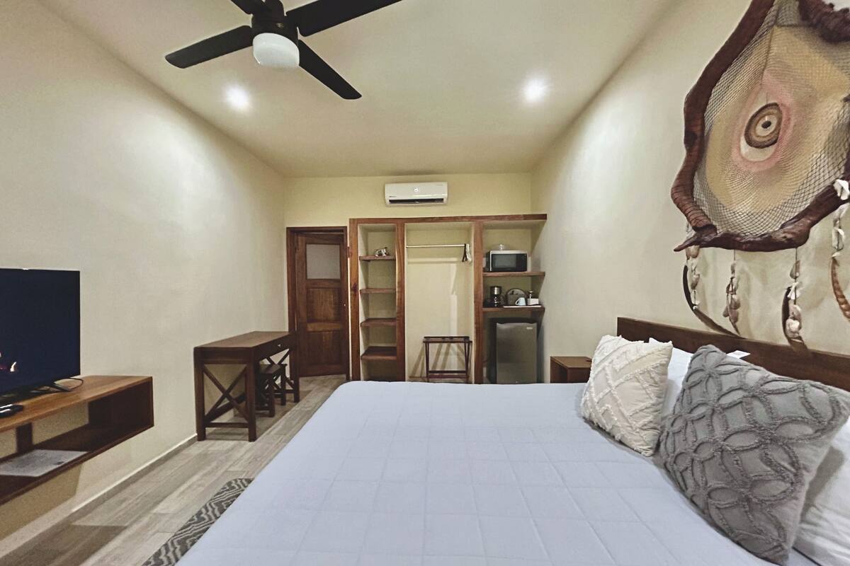 A bedroom with a bed, a desk, a chair, a television, a wardrobe, and a ceiling fan.