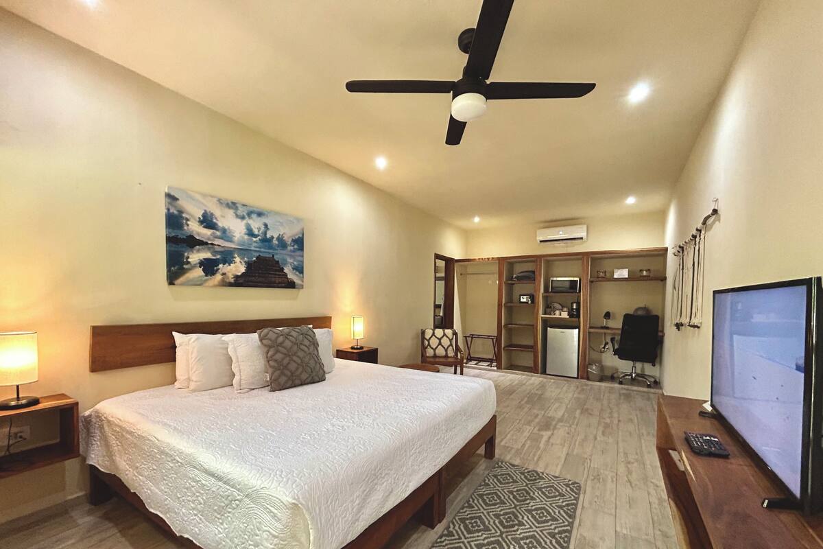 A spacious bedroom with a large bed, a ceiling fan, an air conditioning unit, a television, and a wardrobe.