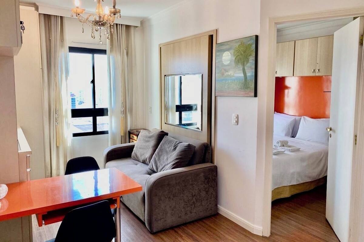 Ein kleines Hotelzimmer mit Sofa, Bett, Essbereich und Blick auf die Stadt durch das Fenster.