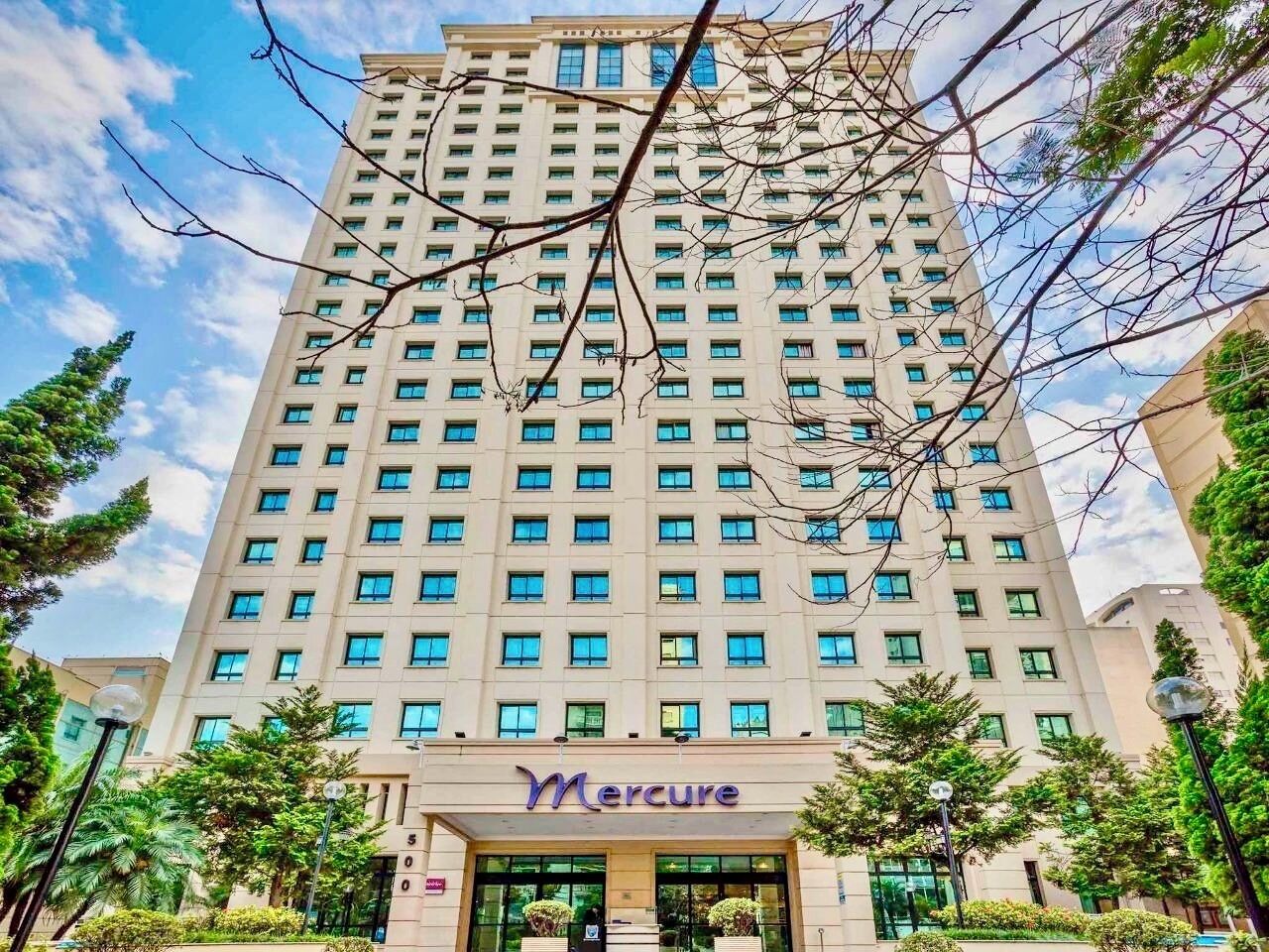 Um hotel alto com um sinal chamativo 'Mercure' na entrada, rodeado por vegetação.