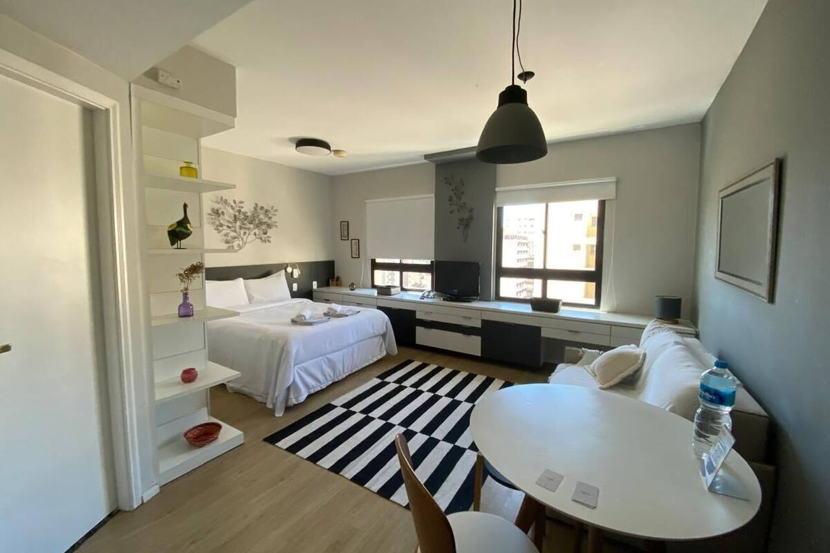 Ein modernes, kompaktes Hotelzimmer mit Bett, Schreibtisch, Stuhl, Esstisch und einem großen Fenster für natürliches Licht.