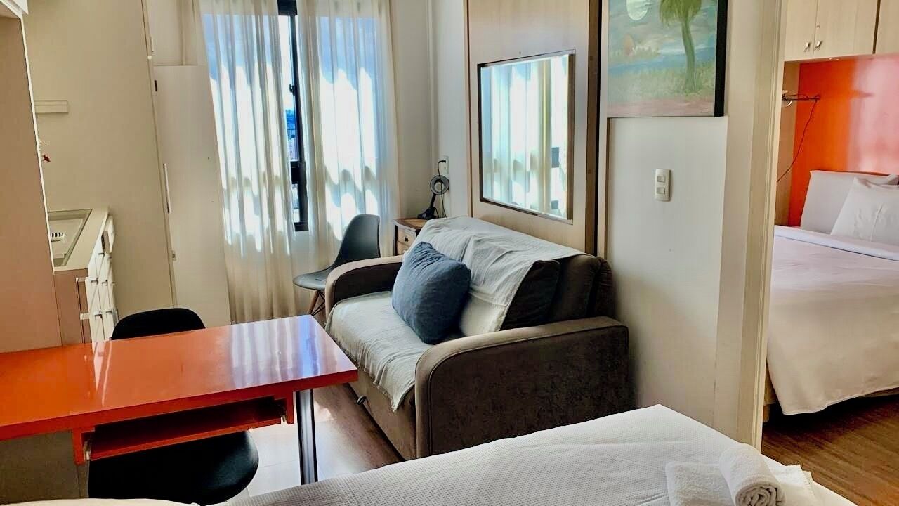 A compact hotel room with a bed, a sofa, a desk, and a chair.