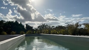 A clear swimming pool with a view of trees and a cloudy sky. - Jungle Escape: Cozy 1-Bedroom Retreat (Tulum)