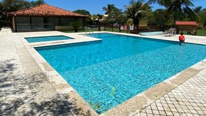 A rectangular swimming pool with a tiled deck, surrounded by palm trees and a covered area with a red roof.