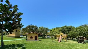 A grassy park area with playground equipment, a small building, and trees.