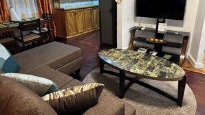 Ein Wohnzimmer mit Sofa, Couchtisch, Fernseher und einer Küchenzeile mit Schränken und Kühlschrank.