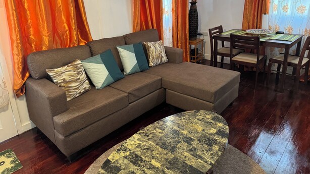 Ein Wohnzimmer mit einem braunen Ecksofa, einem runden Couchtisch und einem Essbereich mit Tisch und Stühlen.