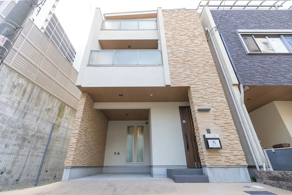 Un bâtiment moderne à deux étages, doté d’une façade en béton, d’une petite entrée avec une porte et d’une petite fenêtre située au-dessus de la porte.